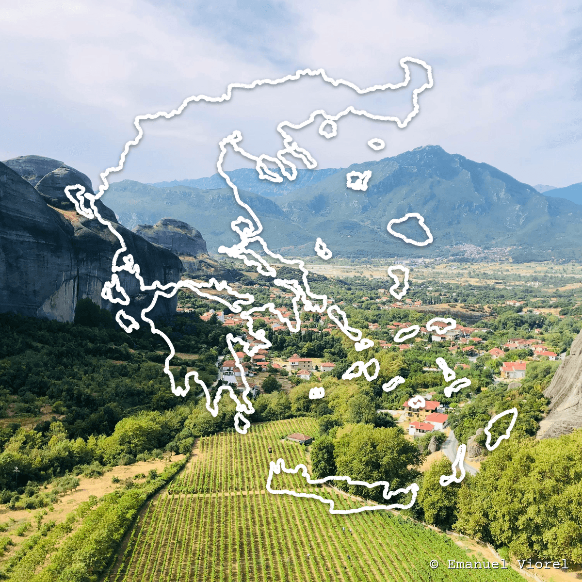 Vineyard in a valley below dramatic rock cliffs and mountains, with the outline of Greece