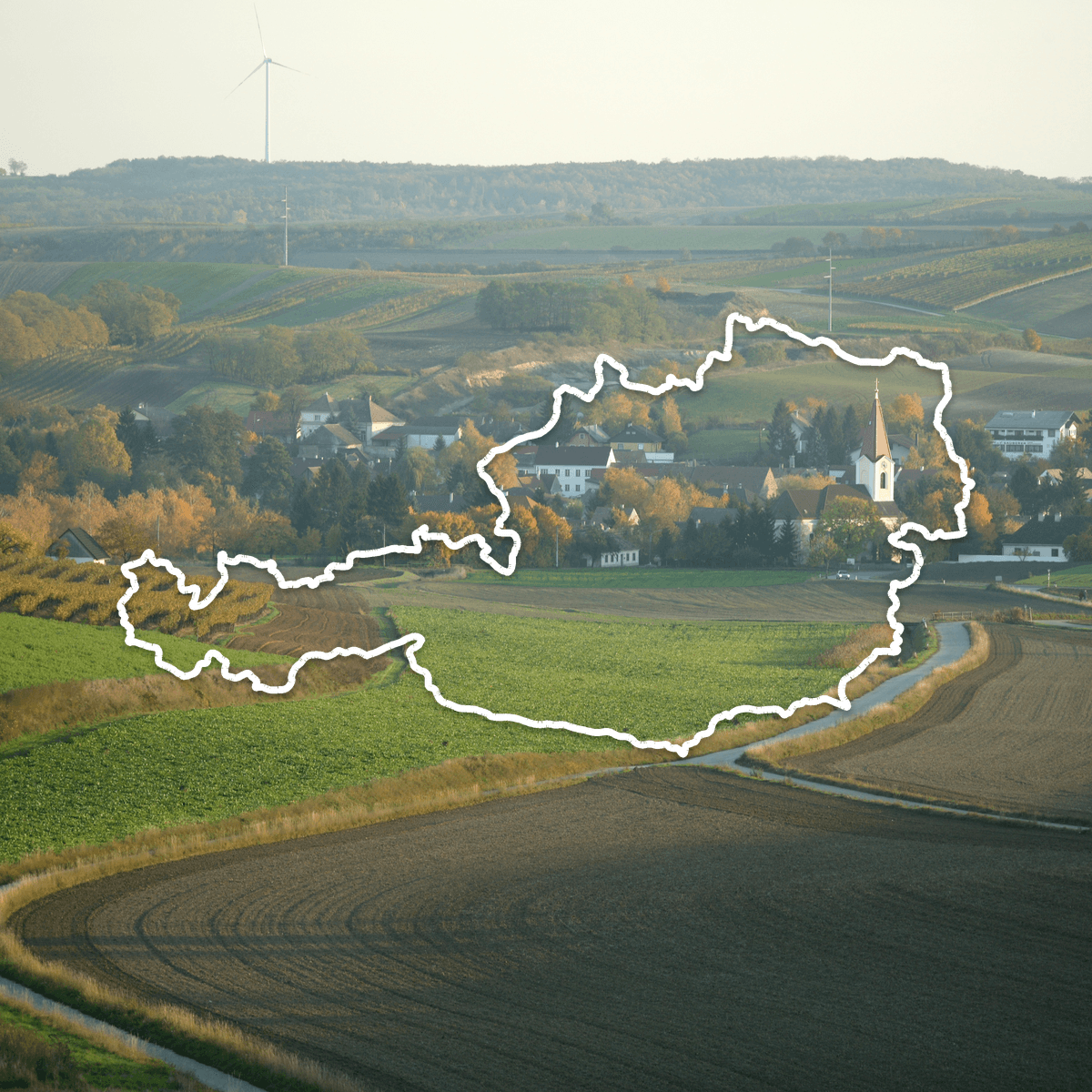 Rolling vineyards and a village church in autumn, with the outline of Austria